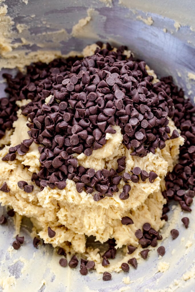 Close up of the bowl of a stand mixer with cookie dough in it with chocolate chips on top.
