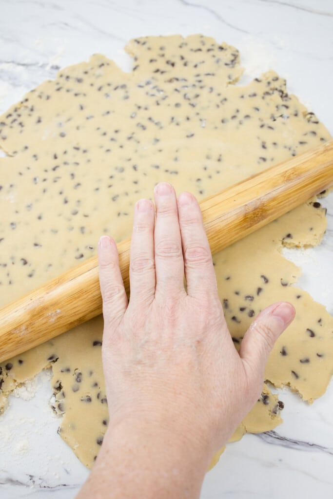 Top view of chocolate chip cookie dough being rolled out with a rolling pin.