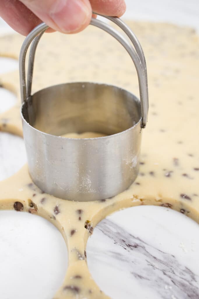 Close up of rolled out chocolate chip cookie dough being cut with a circular cutter.