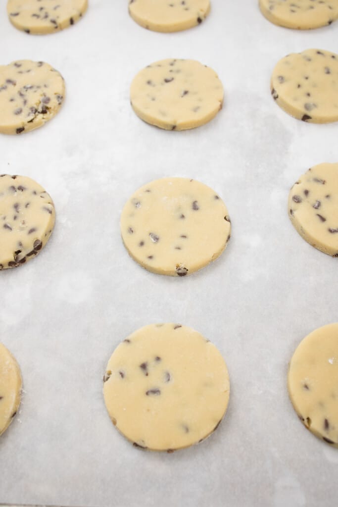 Close up of a baking tray with parchment paper on it with chocolate chip cookie cut outs lined up on it.