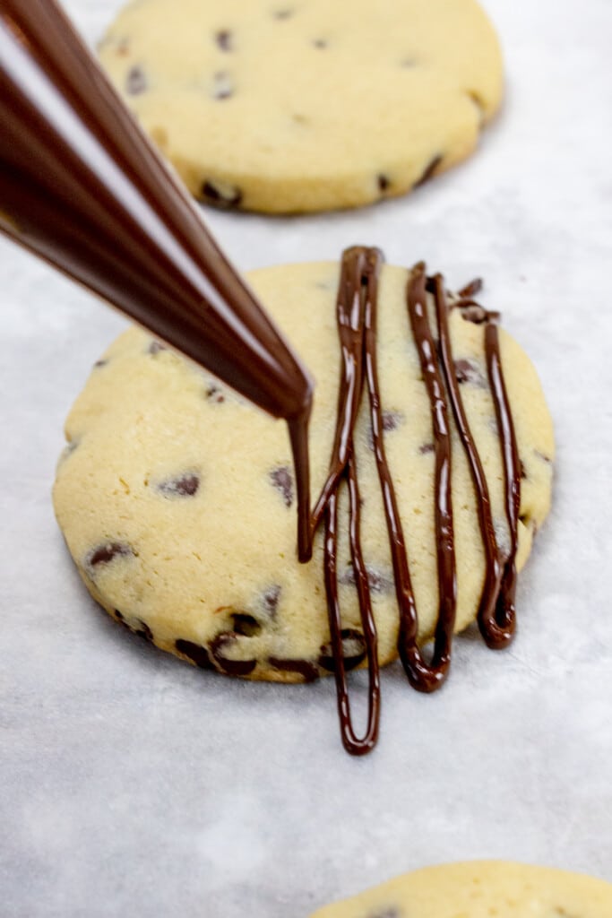 Close up of chocolate chip cookies with melted chocolate being drizzled on top in lines.