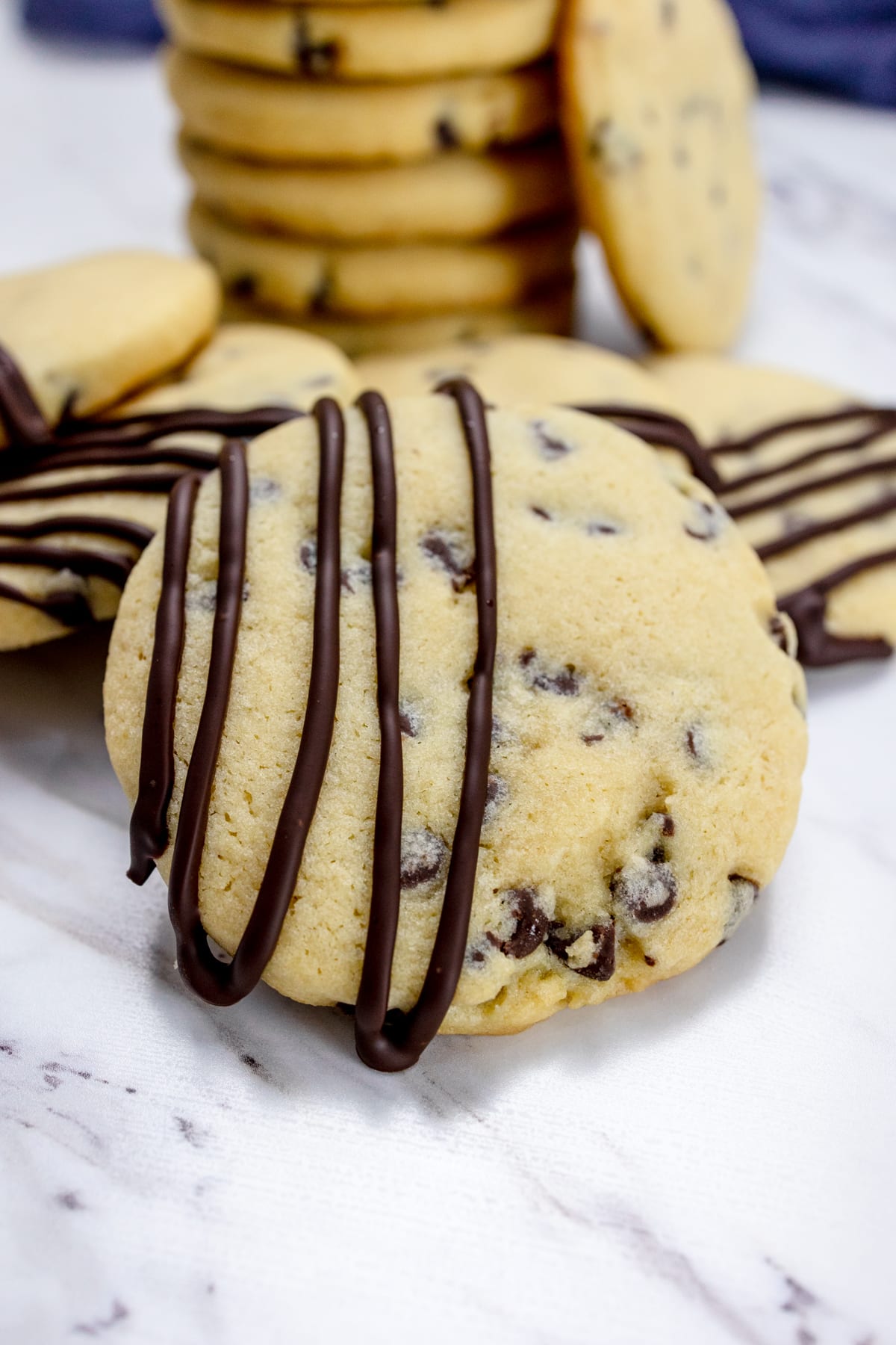 Close up of a chocolate chip cookie with melted chocolate on it in front of a stack of chocolate chip cookies.