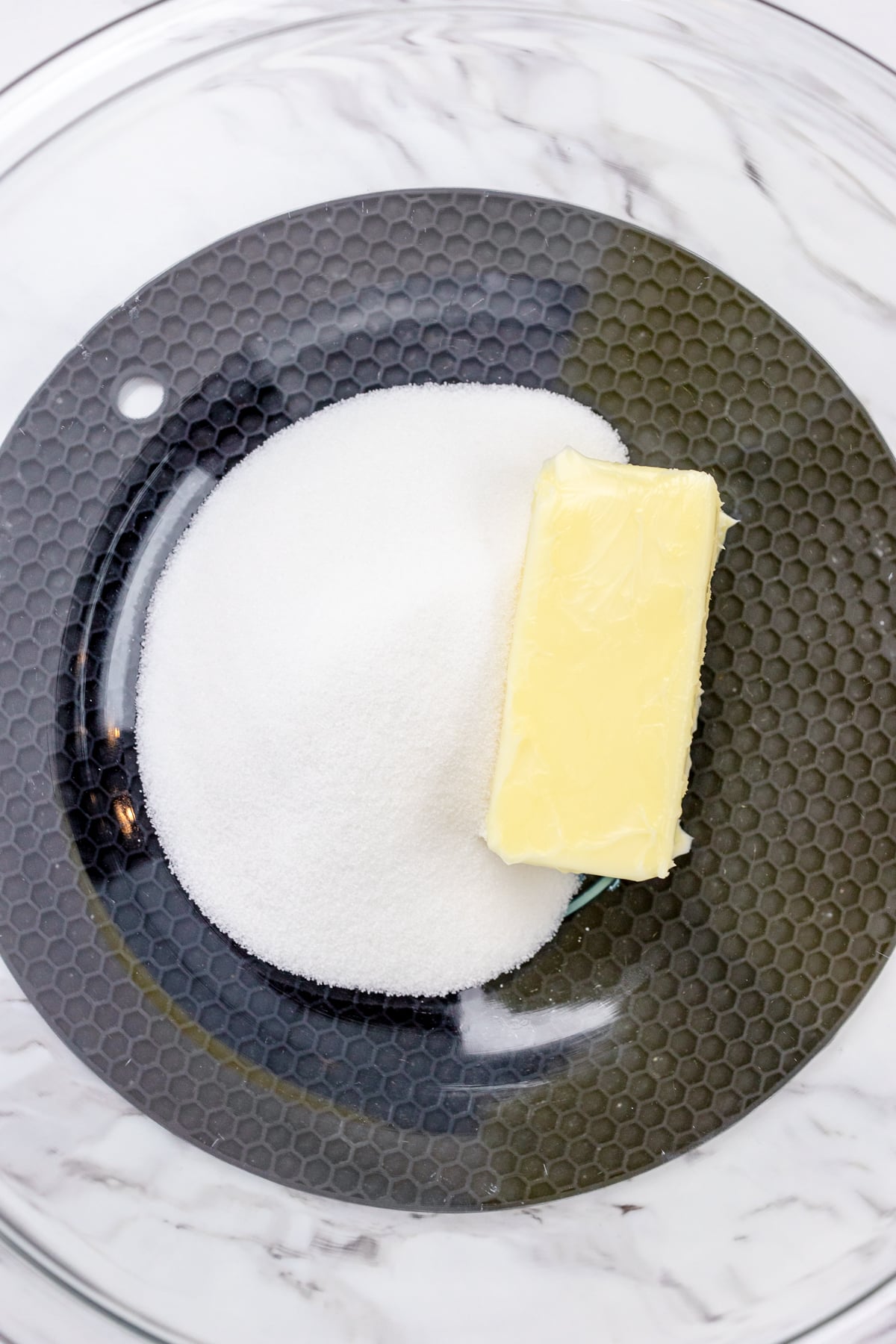 Top view of a mixing bowl with sugar and butter in it.
