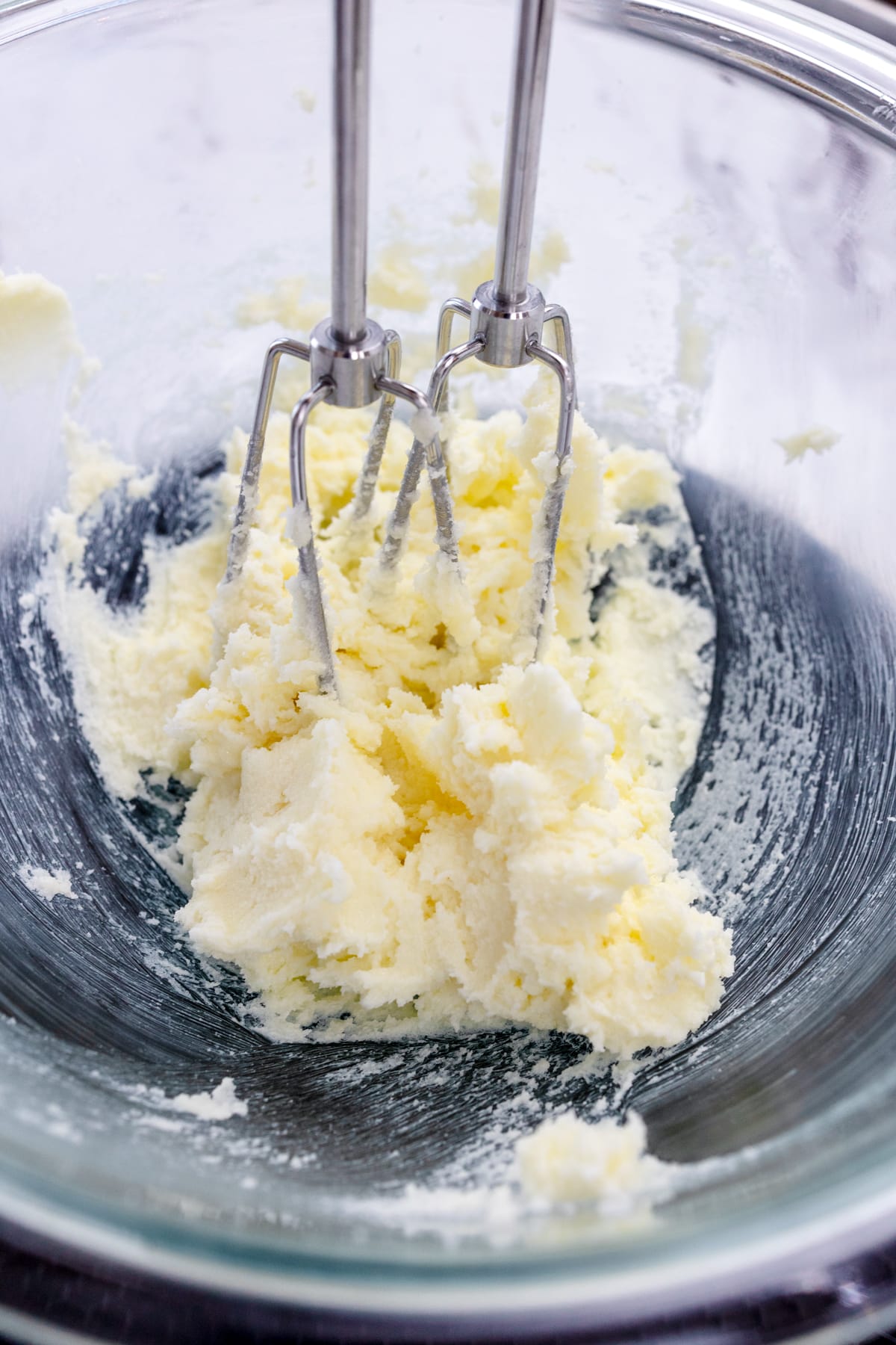 Close up of a mixing bowl containing a creamed mixture with almond extract and milk in it.