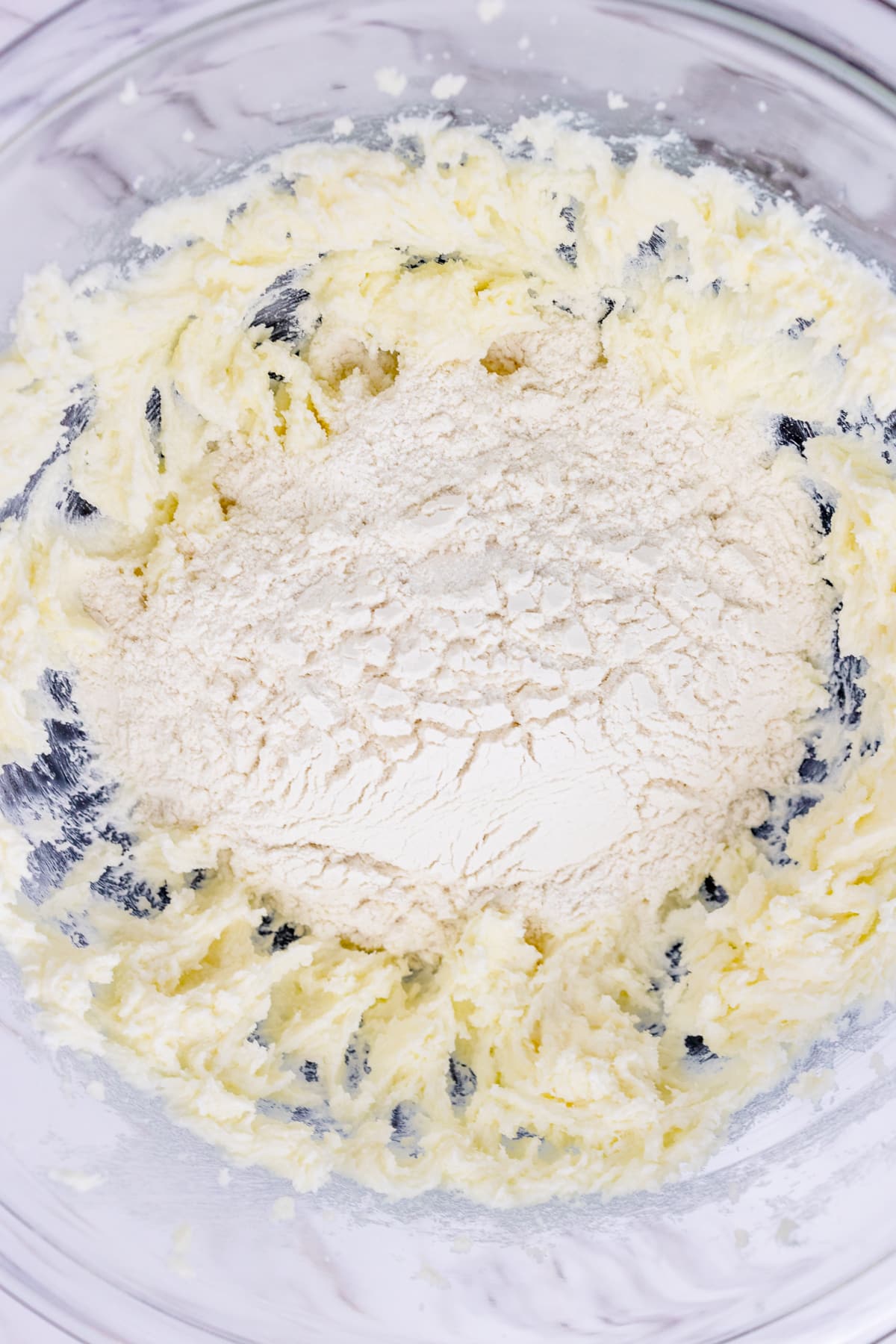 Close up view of a mixing bowl with creamed mixture in it with flour on top ready to be mixed in.
