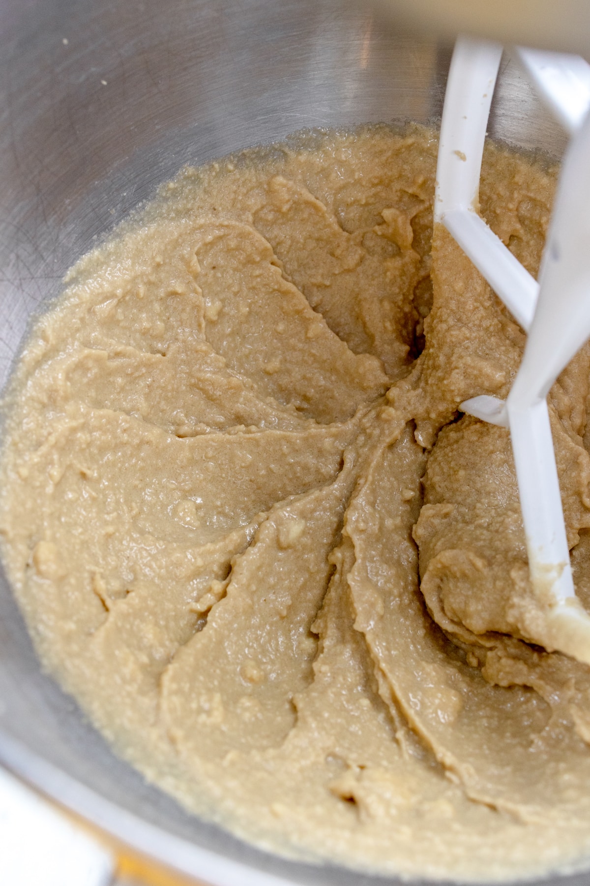 Close up of the bowl of a stand mixer with ingredients being mixed together with a paddle attachment.