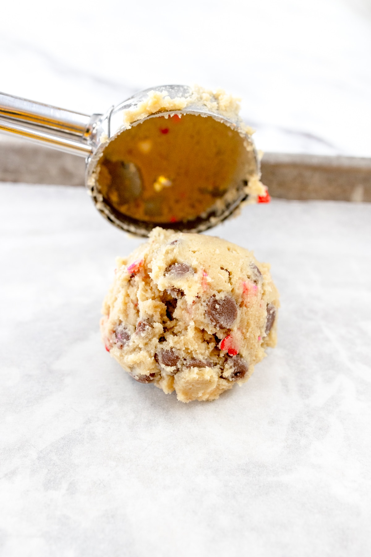 Close up of a cookie scoop placing a scoop of cookie dough onto a baking tray lined with parchment paper