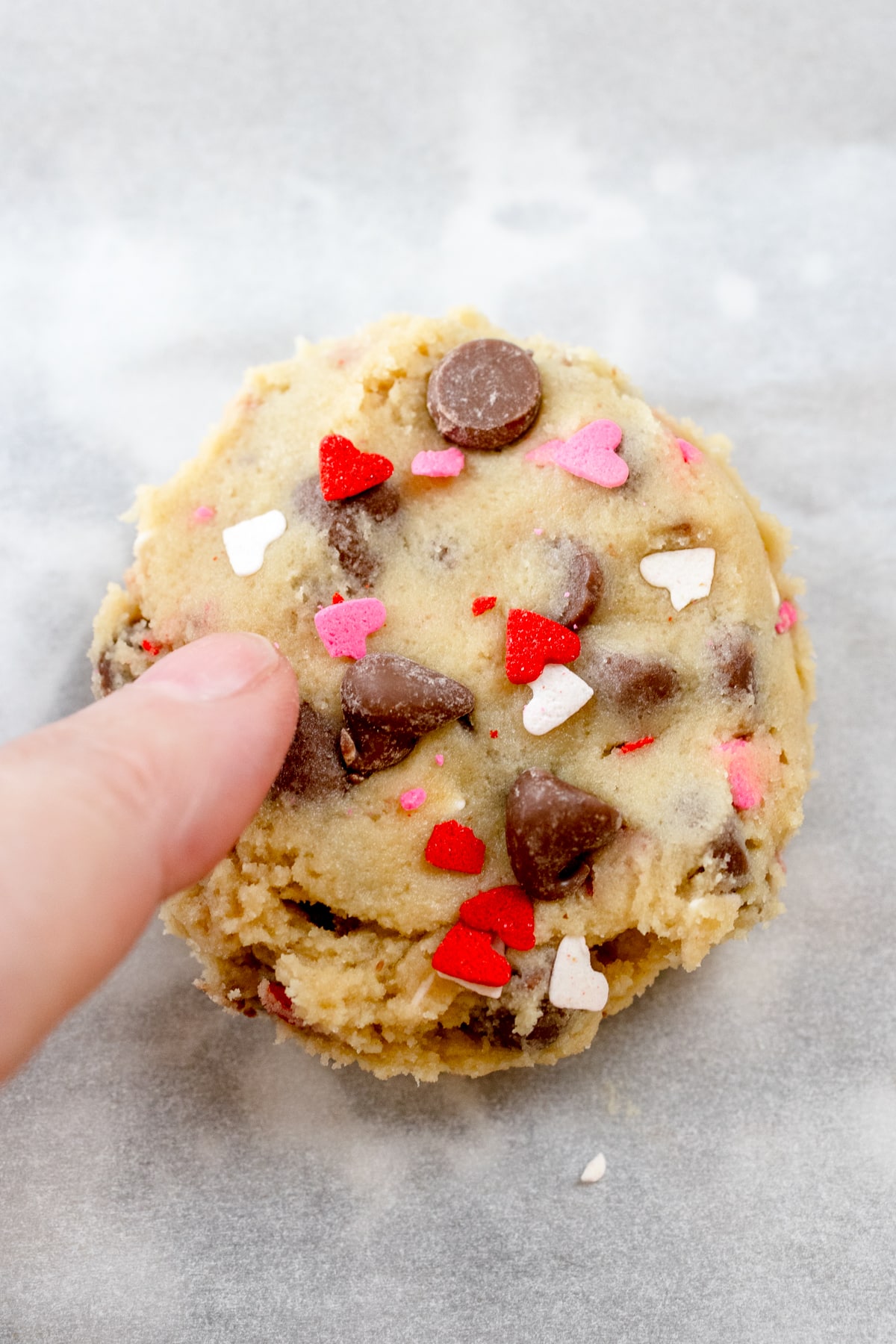 Close up view of a hand pressing extra chocolate chips and sprinkles on top of a cookie dough ball.