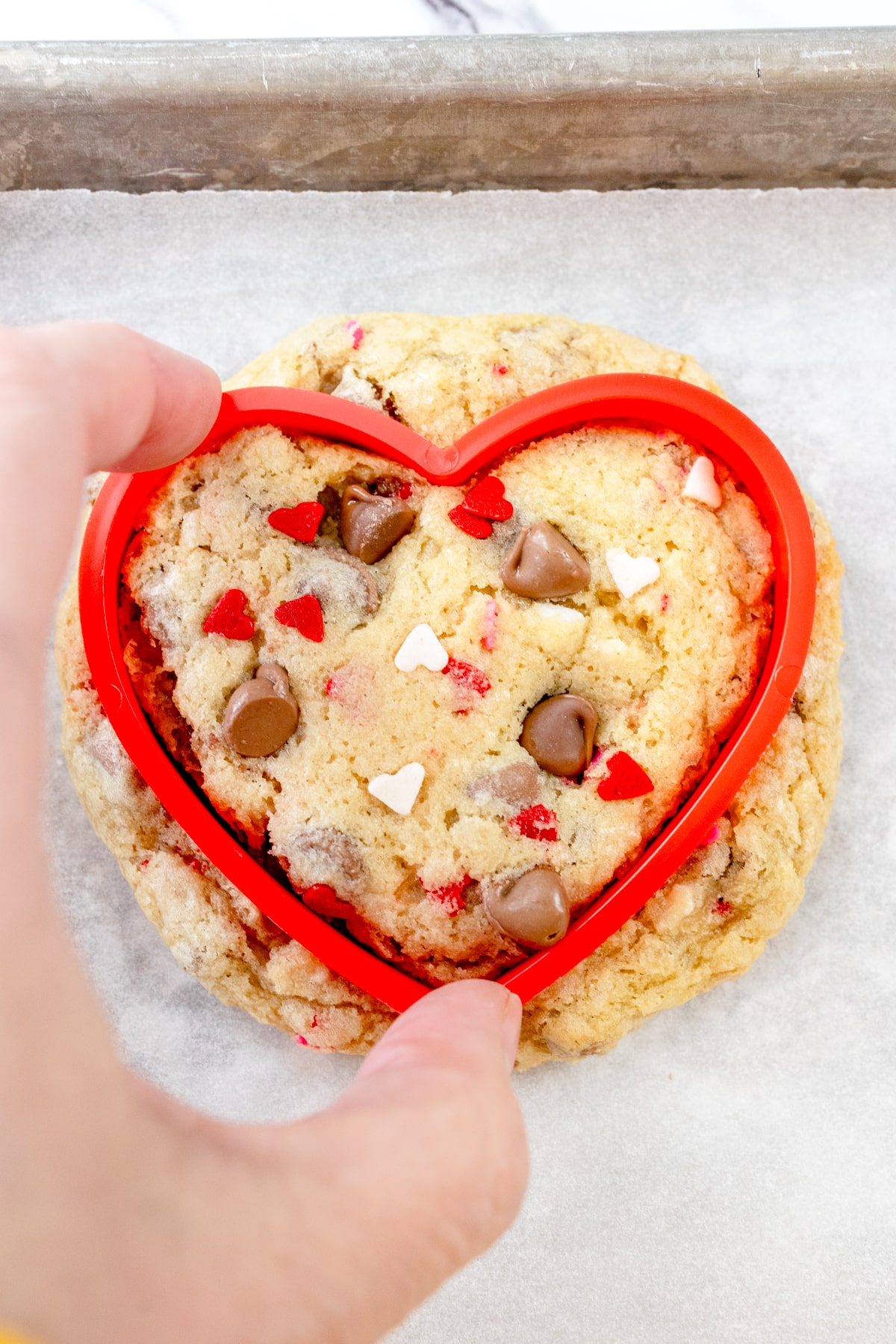 Top view of cookie on a baking tray with a heart-shaped cutter placed over it.