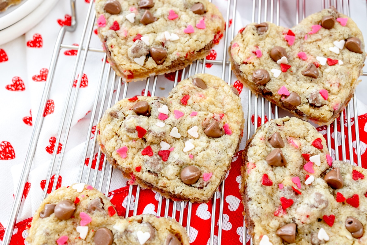 Close up view of heart shaped cookies on a wire rack with love heart decorations around the cookies.