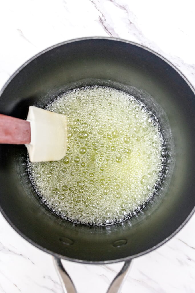 Top view of a spatula stirring melted butter in a frying pan.