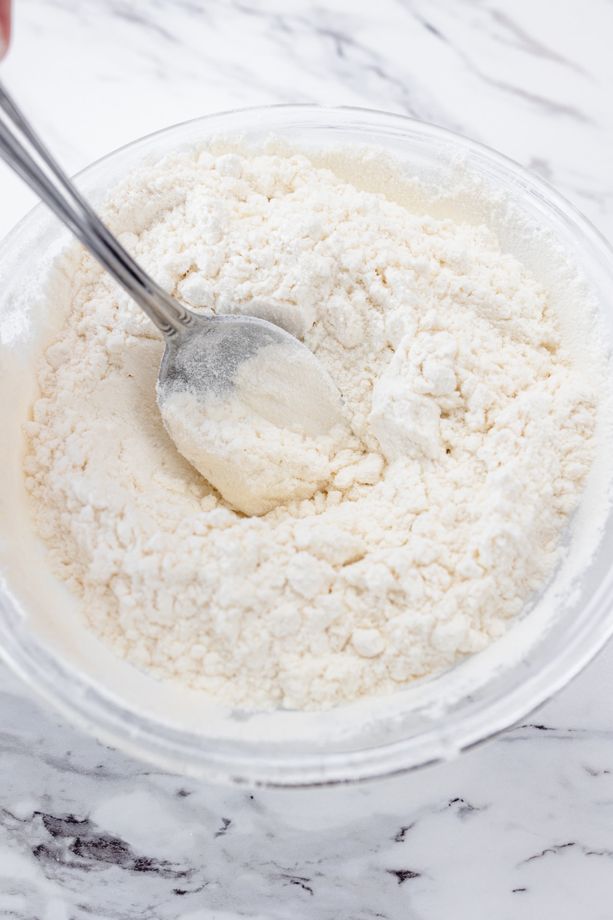 Close up view of flour in a microwavable bowl being stirred with a spoon.