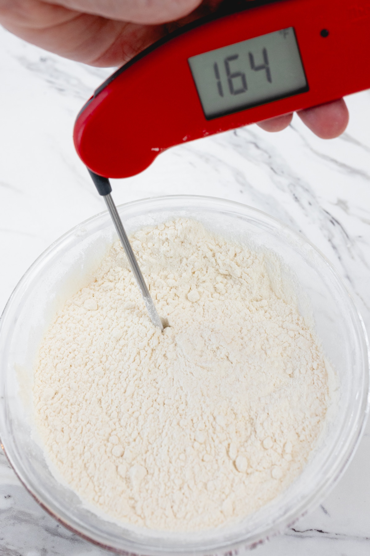 Close up view of flour in a microwavable bowl with a thermometer inserted below the surface.