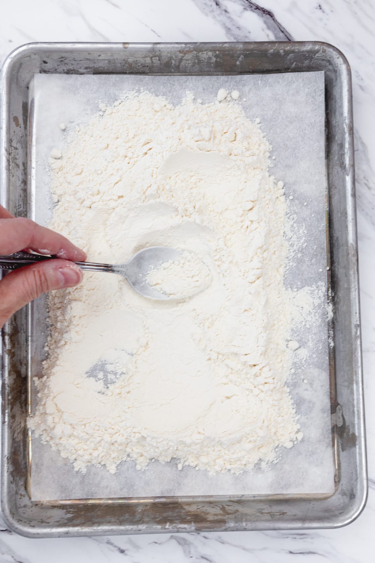 Top view of flour being spread on a parchment-lined baking sheet.