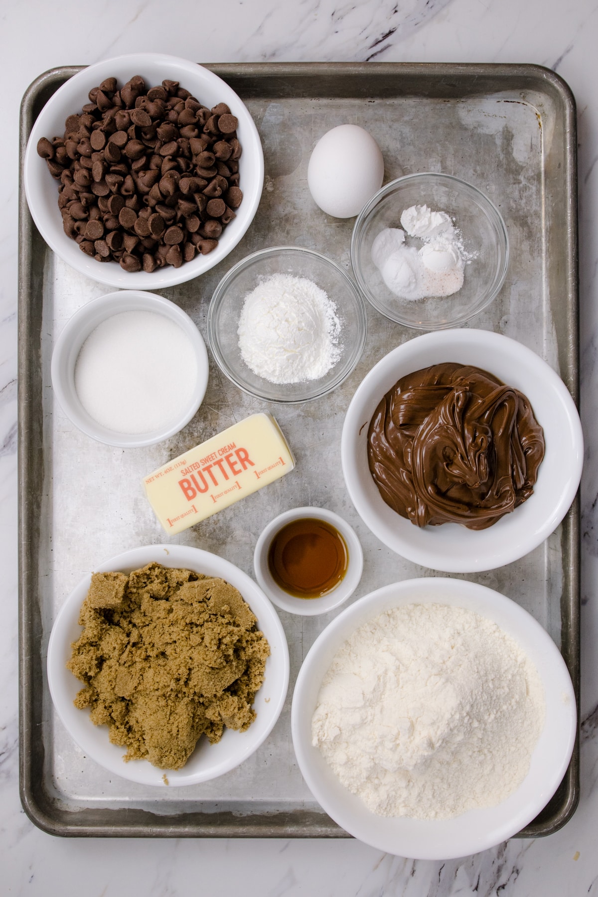 Top view of ingredients needed to make Nutella Cookies in small bowls on a baking tray.