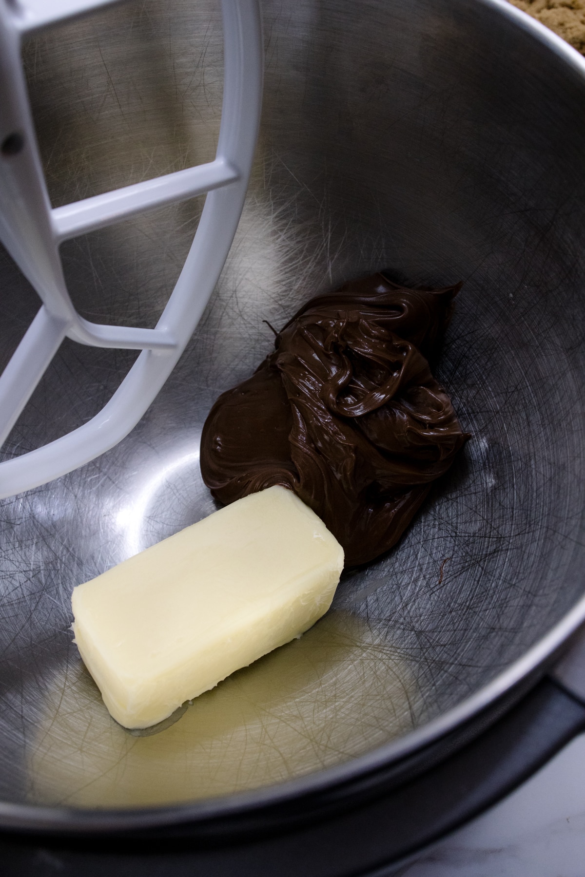 Close up of the bowl of a stand mixer with butter and Nutella being creamed together with a paddle attachment.