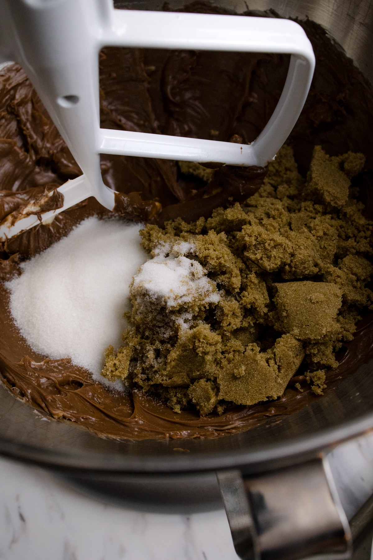Close up of the bowl of a stand mixer with butter mixture and sugars being creamed together with a paddle attachment.