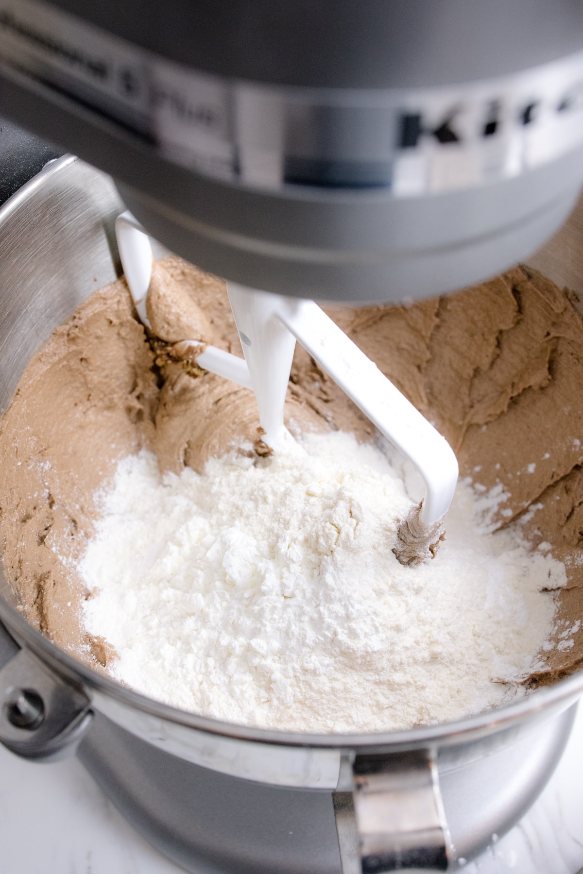 Close up of the bowl of a stand mixer with dry and wet ingredients ready to be mixed together with a paddle attachment.