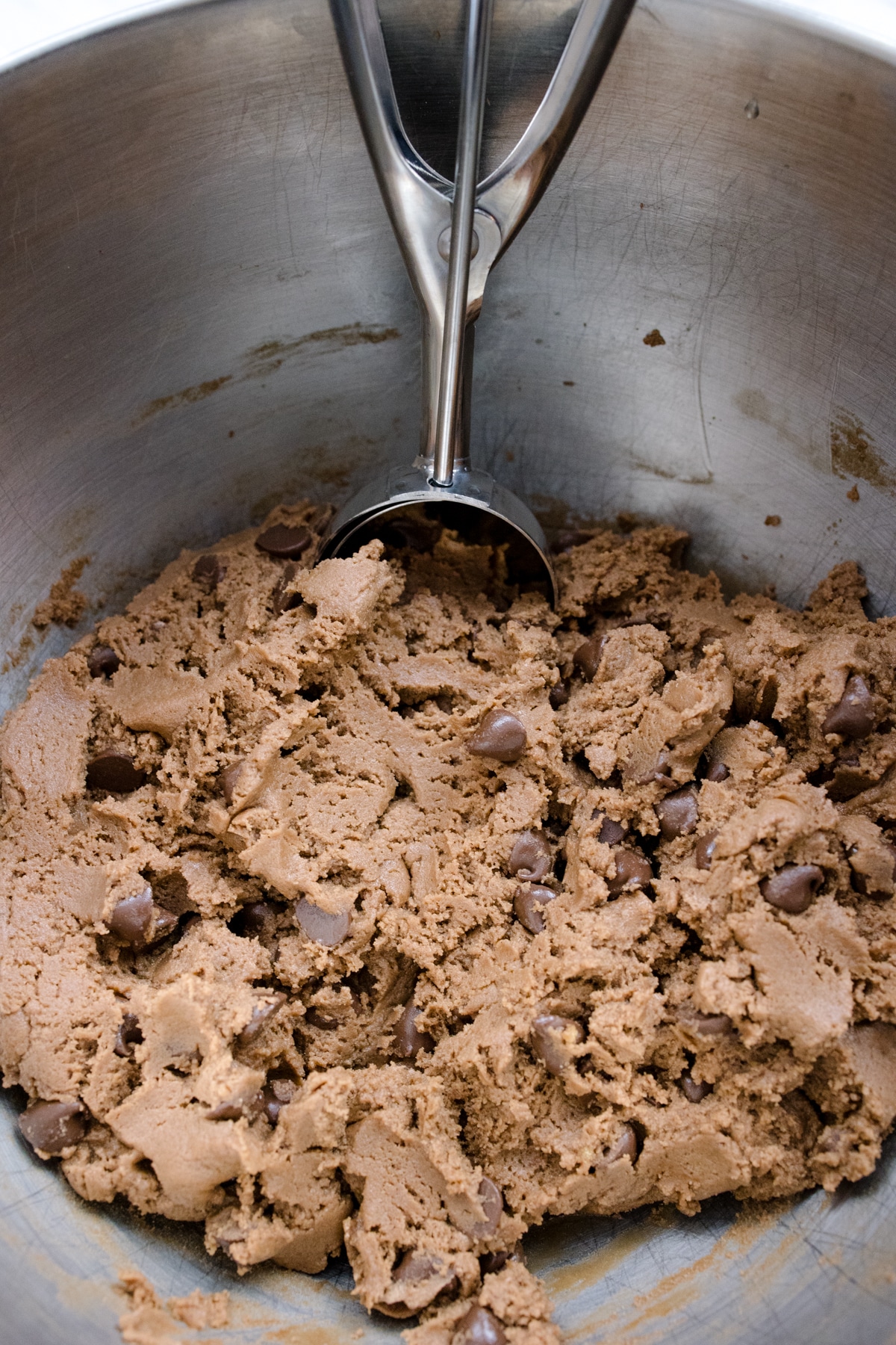 Close up of the bowl of a stand mixer with cookie dough in it and a scoop inserted.
