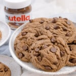 Angled view of Nutella Cookies on several white plates, on a white surface, with a jar of Nutella in the background.