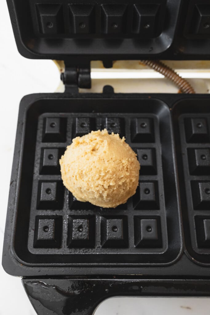 Close up of a scoop of waffle cookie dough on a greased waffle iron.