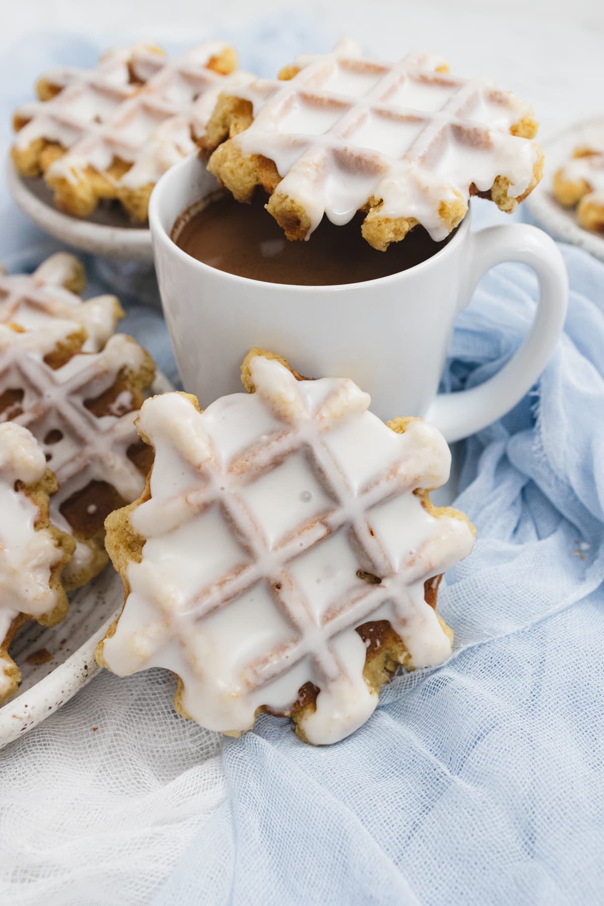 Close up of a white cup of coffee with a waffle cookie on top with a waffle cookie leaning against the mug.