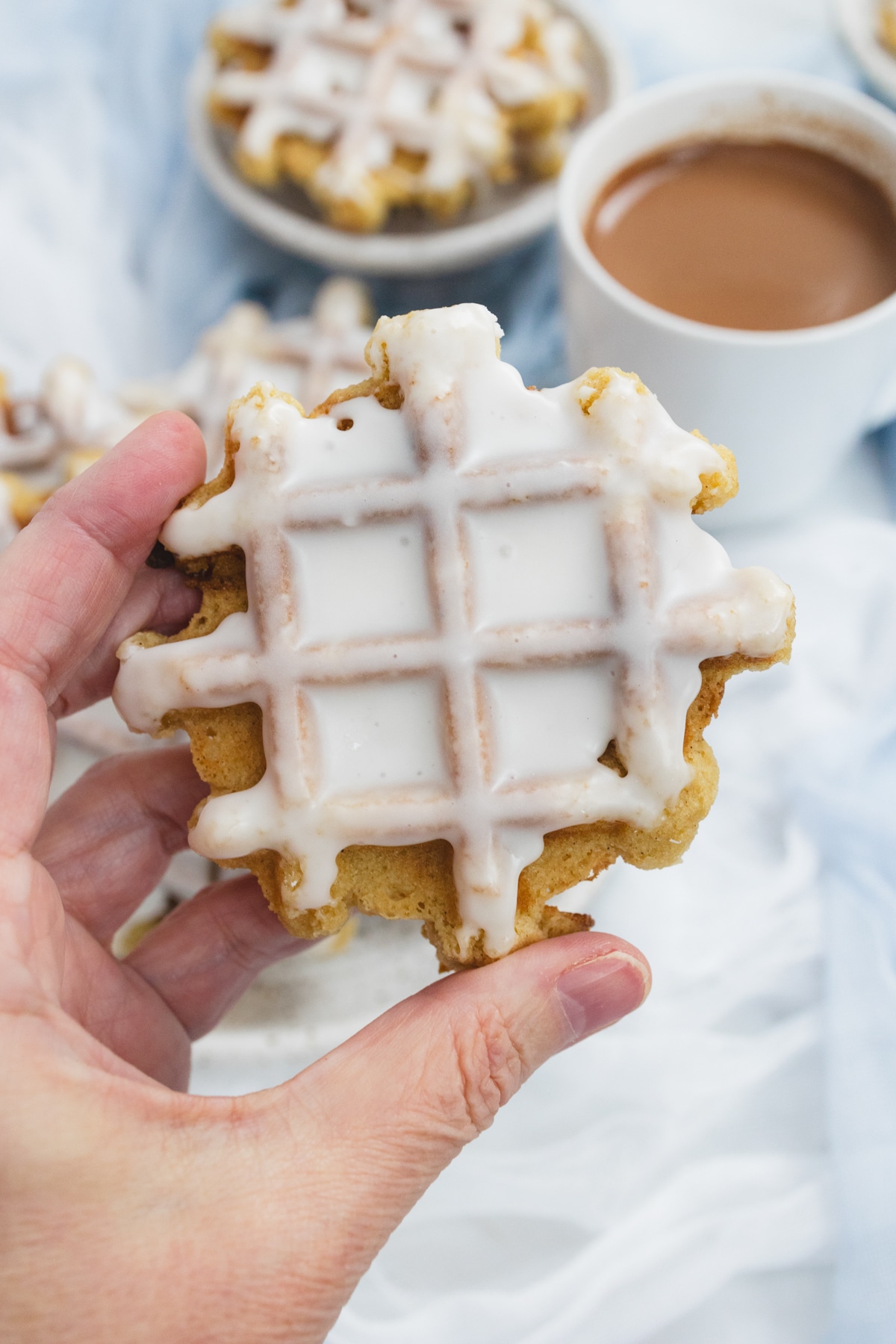 Top view close up of a waffle cookie coated in powdered sugar being held in mid-air.