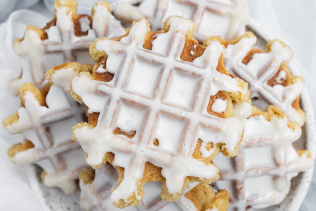 Top view of waffle cookies with icing on them in a pile on a plate.