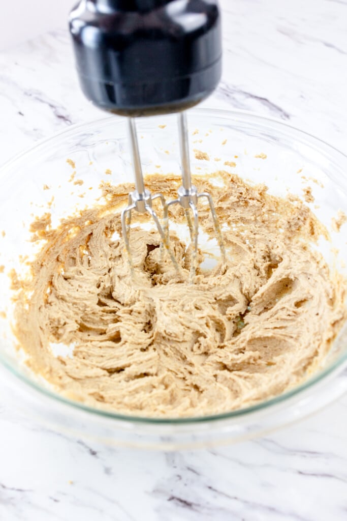 Close up view of an electric hand mixer mixing together vanilla extract with the peanut butter mixture.