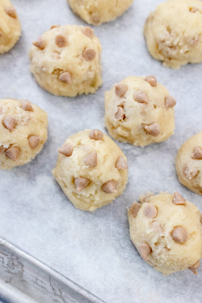 Close view of baking tray lined with parchment paper with Cookie dough balls on it.