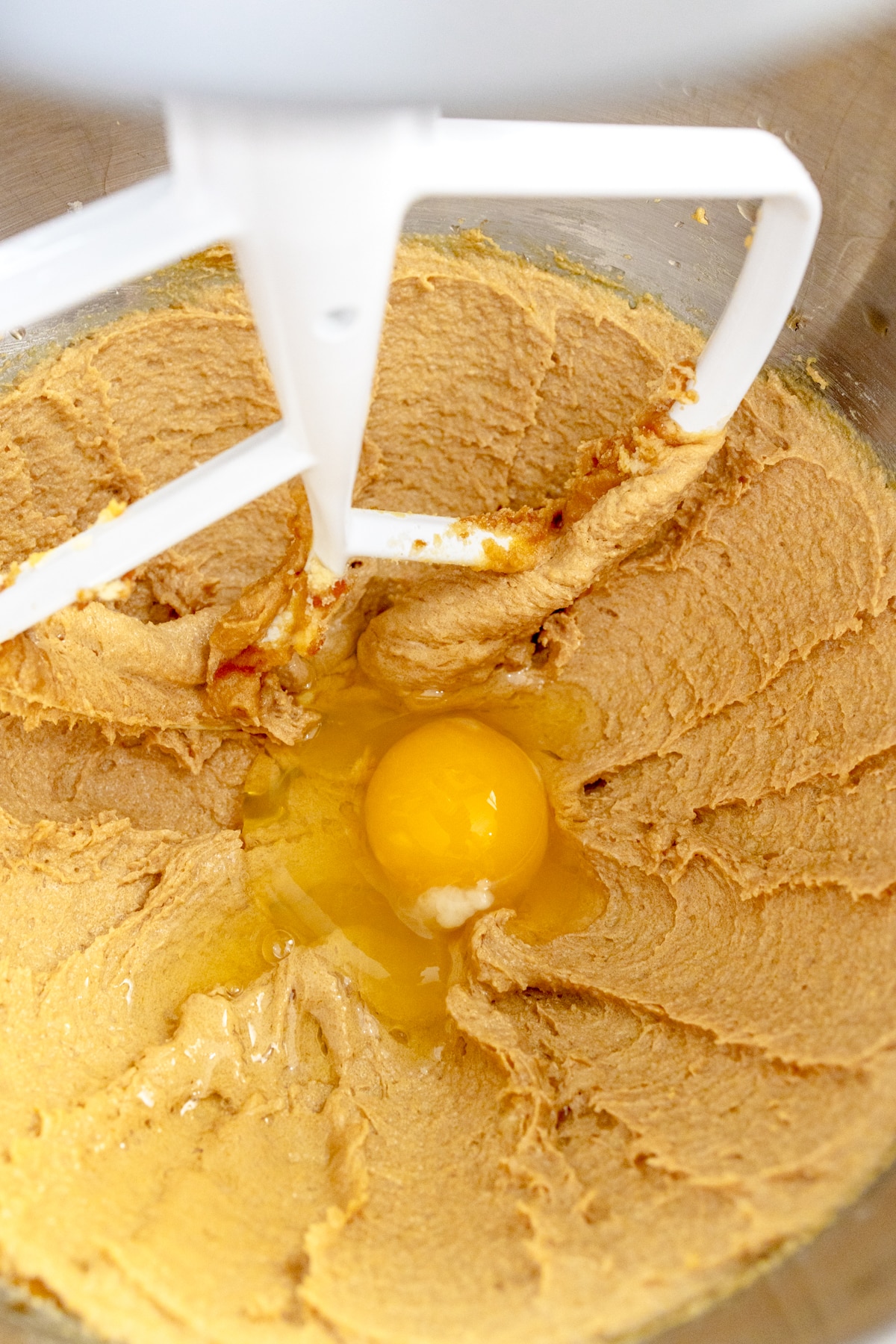 Close up of the bowl of a stand mixer with a creamed mixture in it with an egg on top.