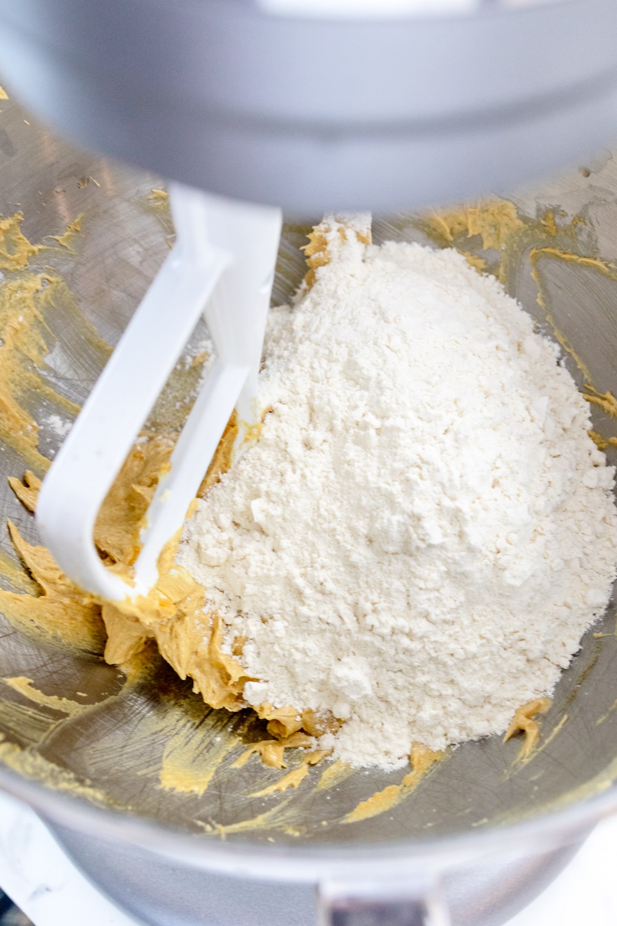 Close up of the bowl of a stand mixer with dry and wet ingredients ready to be mixed together with a paddle attachment.