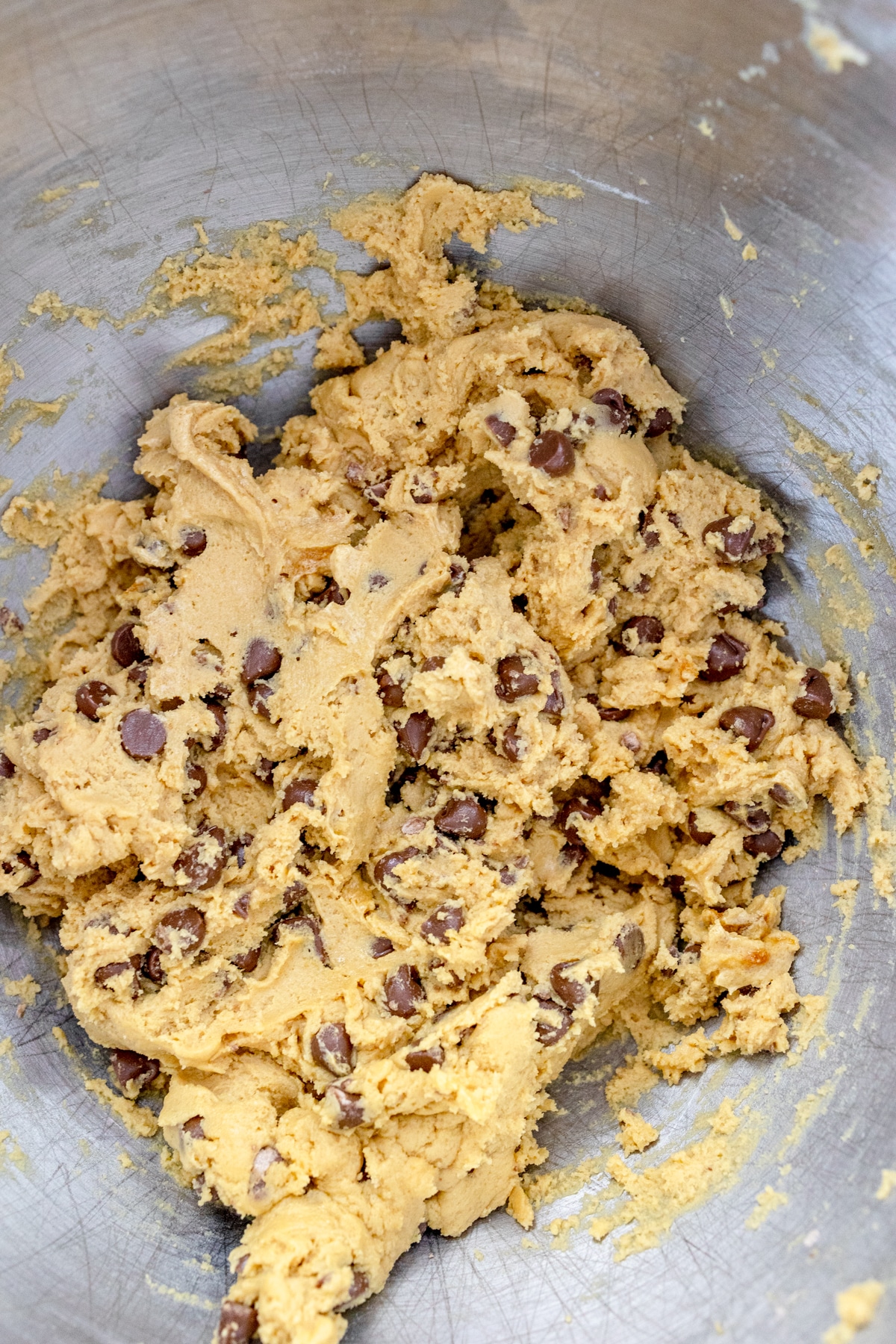 Close up of a metal mixing bowl with chocolate chip cookie dough in it.