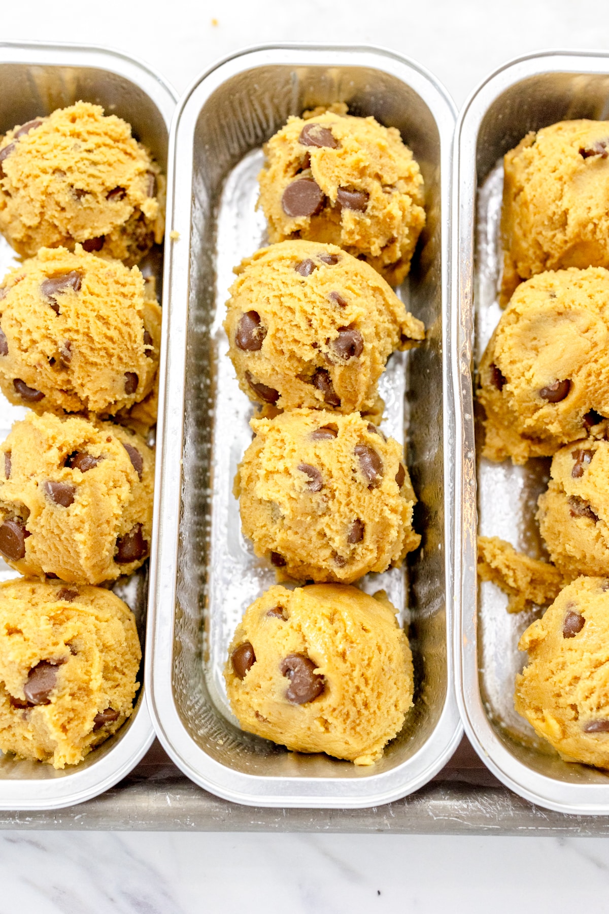 Close up of three footlong baking tins with four chocolate chip cookie dough balls in each.