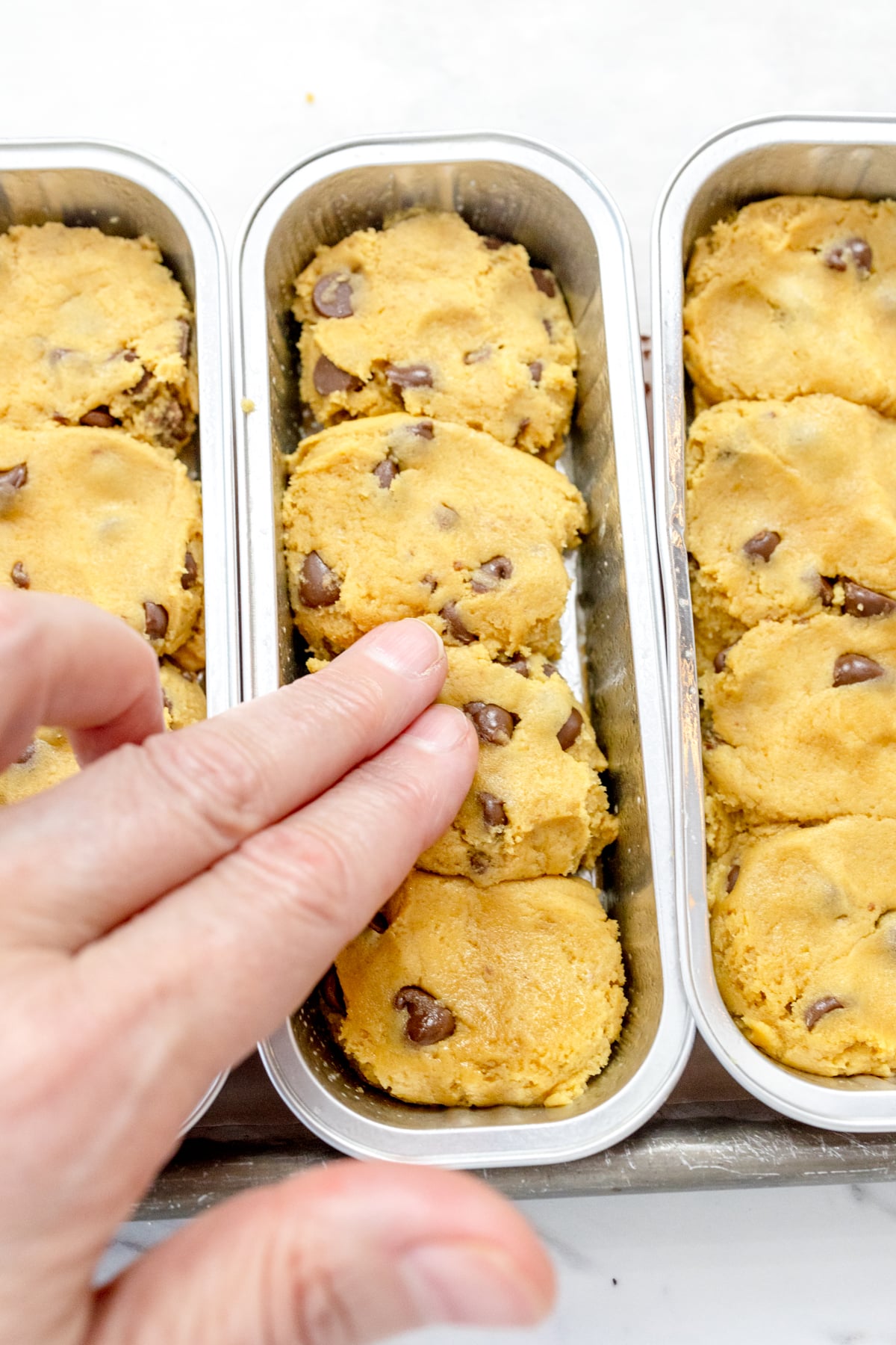 Close up of a hand pressing down cookie dough in three footlong baking tins.