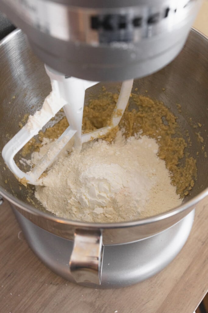 Close up of the bowl of a stand mixer with dry and wet ingredients ready to be mixed together with a paddle attachment.