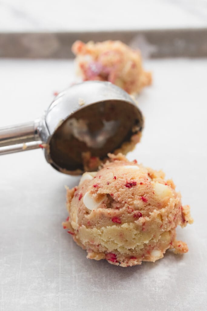 Close up of a cookie scoop placing a scoop of cookie dough onto a baking tray lined with parchment paper