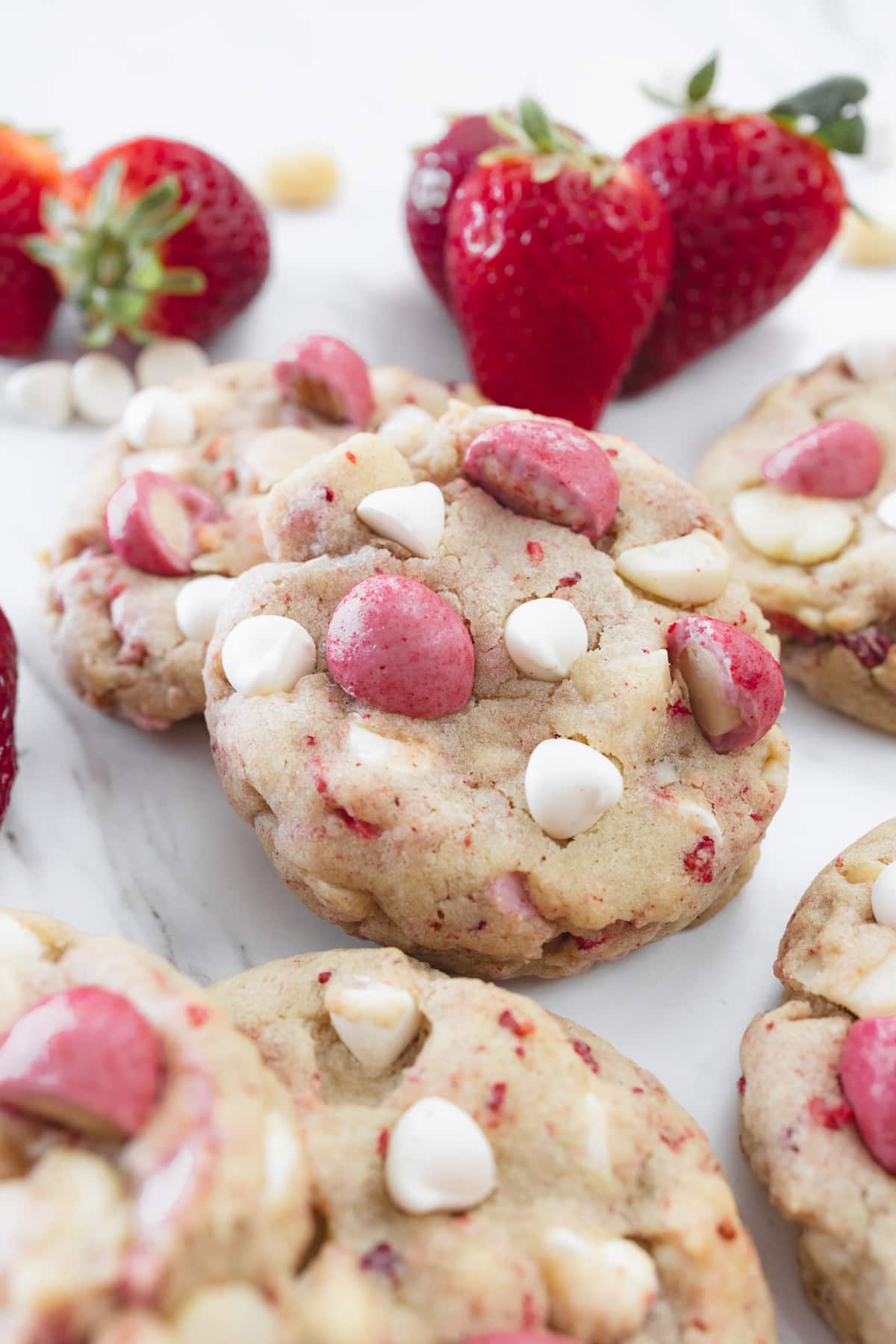 Close up view of Strawberry White Chocolate Macadamia Nut Cookies on a white surface with decorations around.