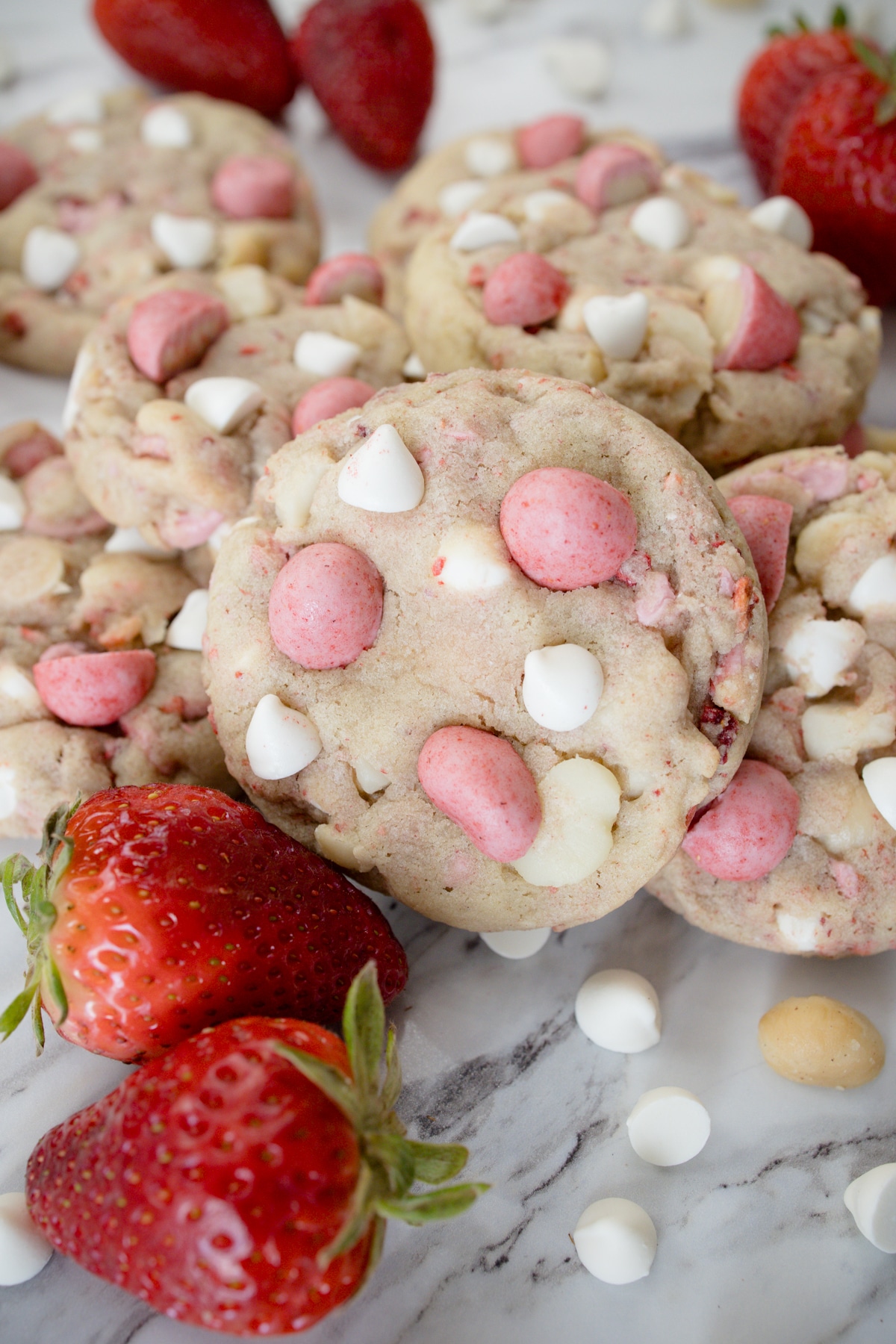 Close up view of Strawberry White Chocolate Macadamia Nut Cookies on a white surface with decorations around.