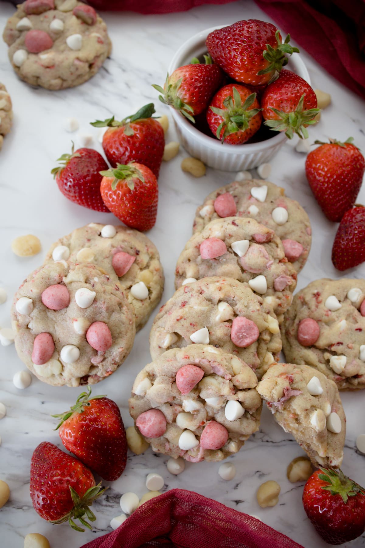 Close up view of Strawberry White Chocolate Macadamia Nut Cookies on a white surface with decorations around.