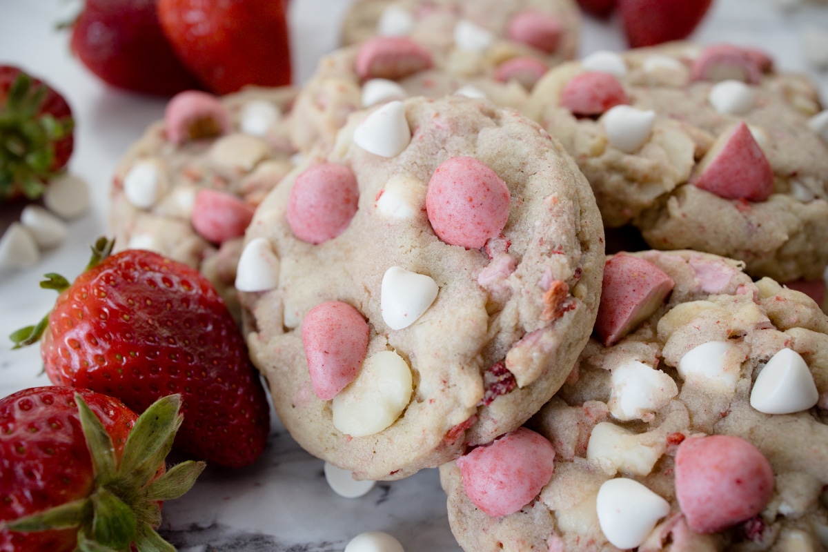 Close up view of Strawberry White Chocolate Macadamia Nut Cookies on a white surface with decorations around.