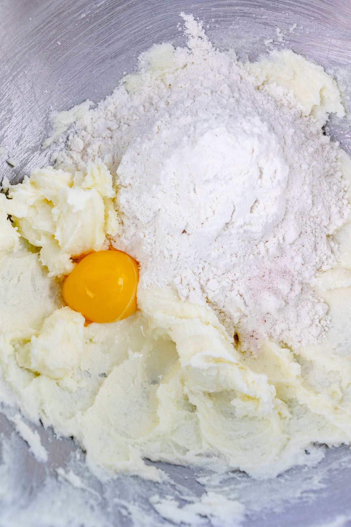 Close up of the bowl of a stand mixer with a creamed mixture in it with flour and an egg on top.