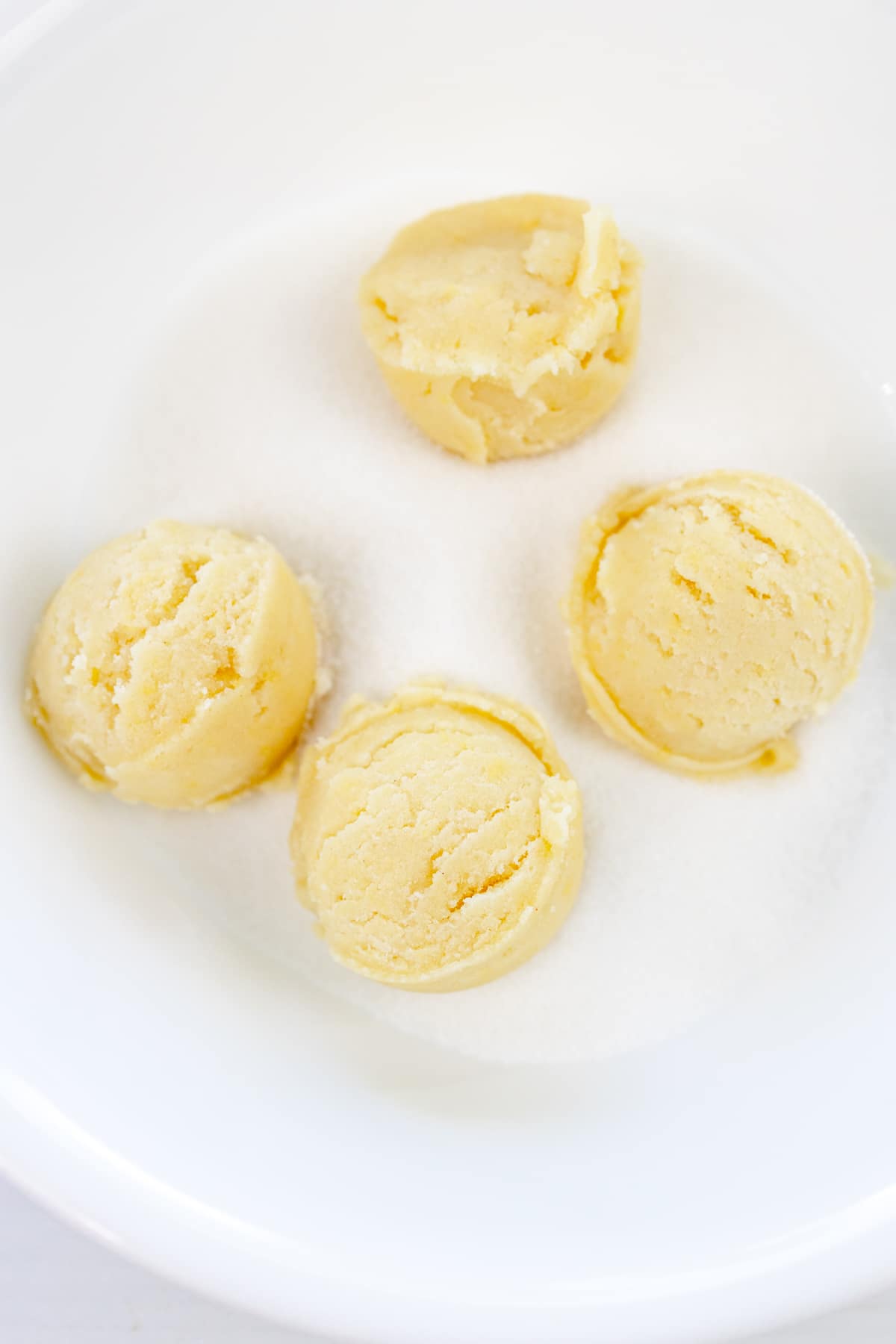 Overhead view of scooped cookie dough balls being rolled in Granulated Sugar.