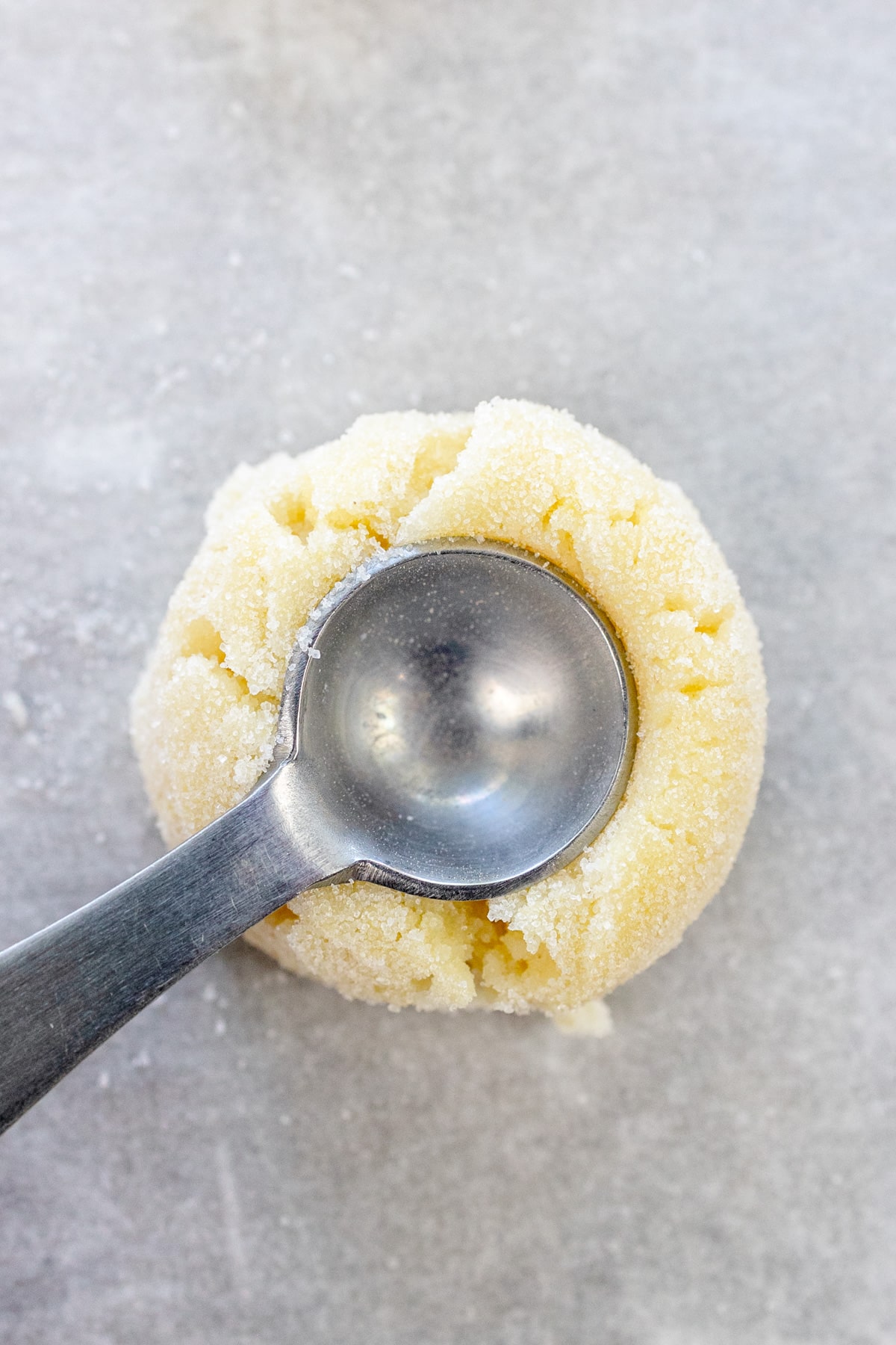 Close up image of a small scoop being used to create a cup in a ball of cookie dough.