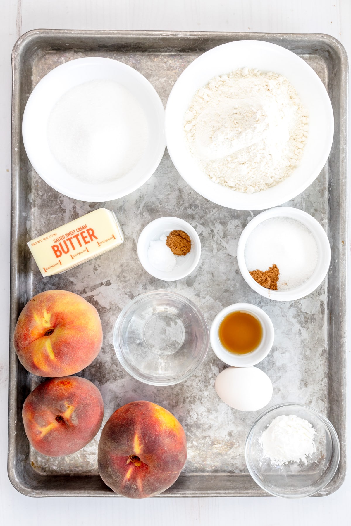 Overhead image of ingredients needed to make Peach Pie Bars in small bowls on a baking tray.