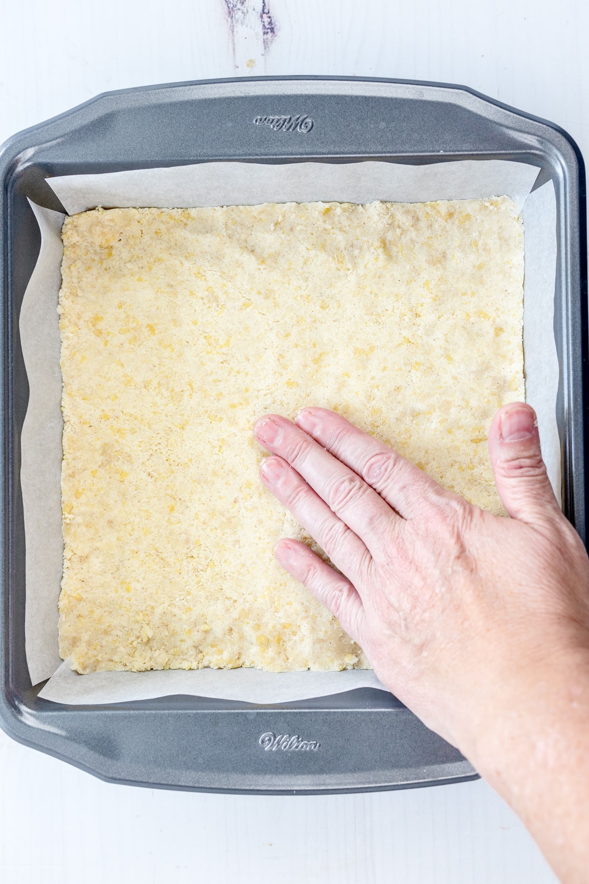 Overhead image of a hand pressing pie crust mixture for Peach Pie Bars into the dish.