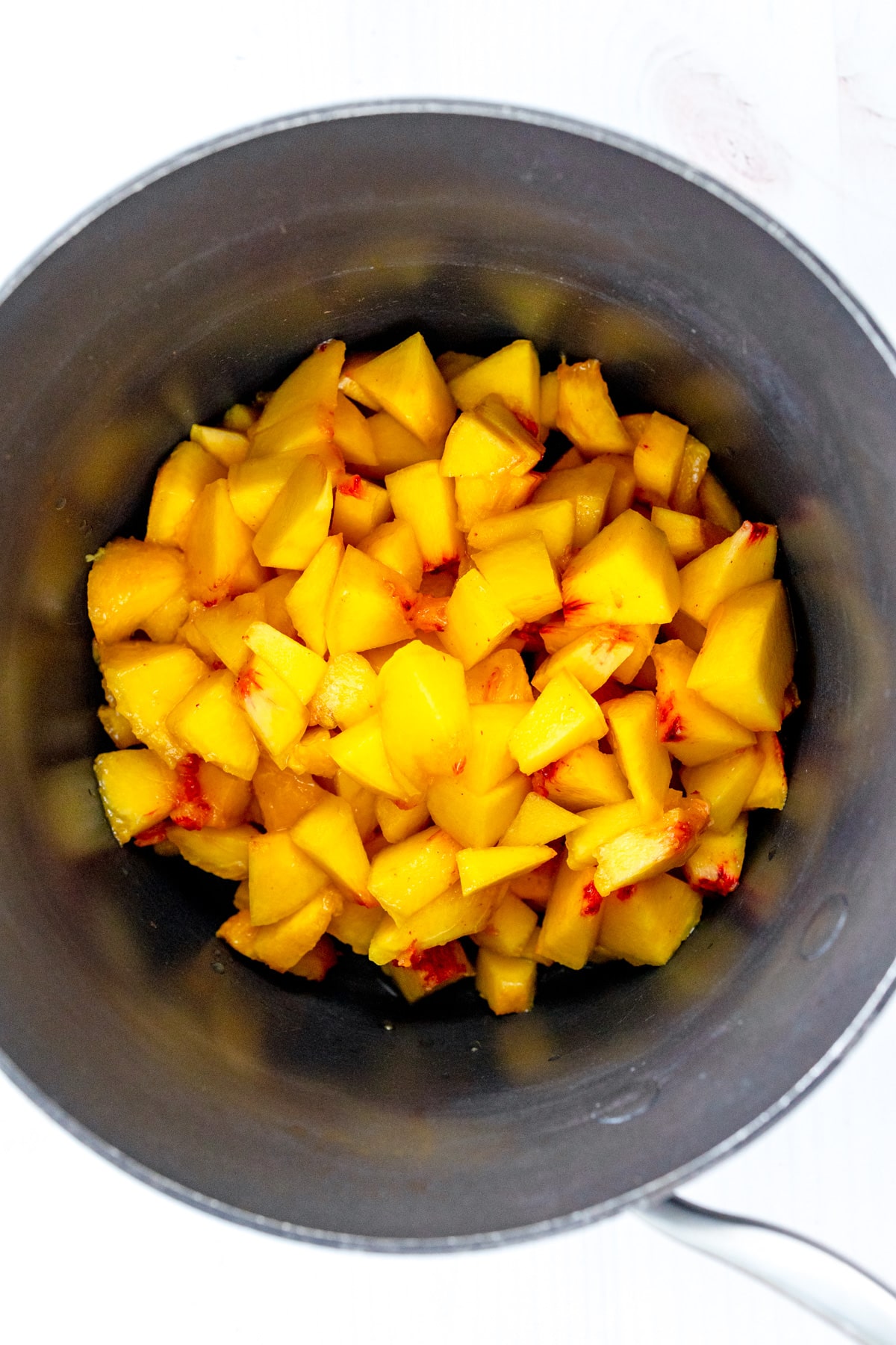 Overhead image of saucepan with sliced peaches for Peach Pie Bars in it.