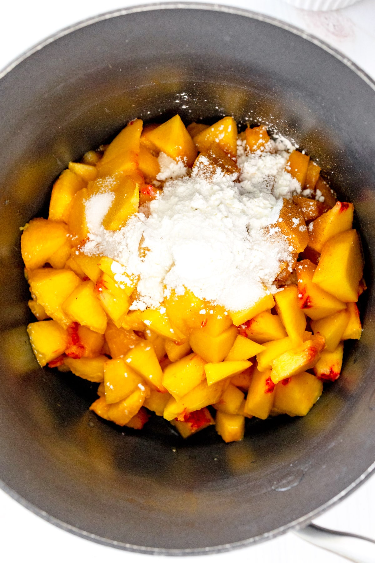 Overhead image of saucepan with sliced peaches and filling ingredients for Peach Pie Bars in it.