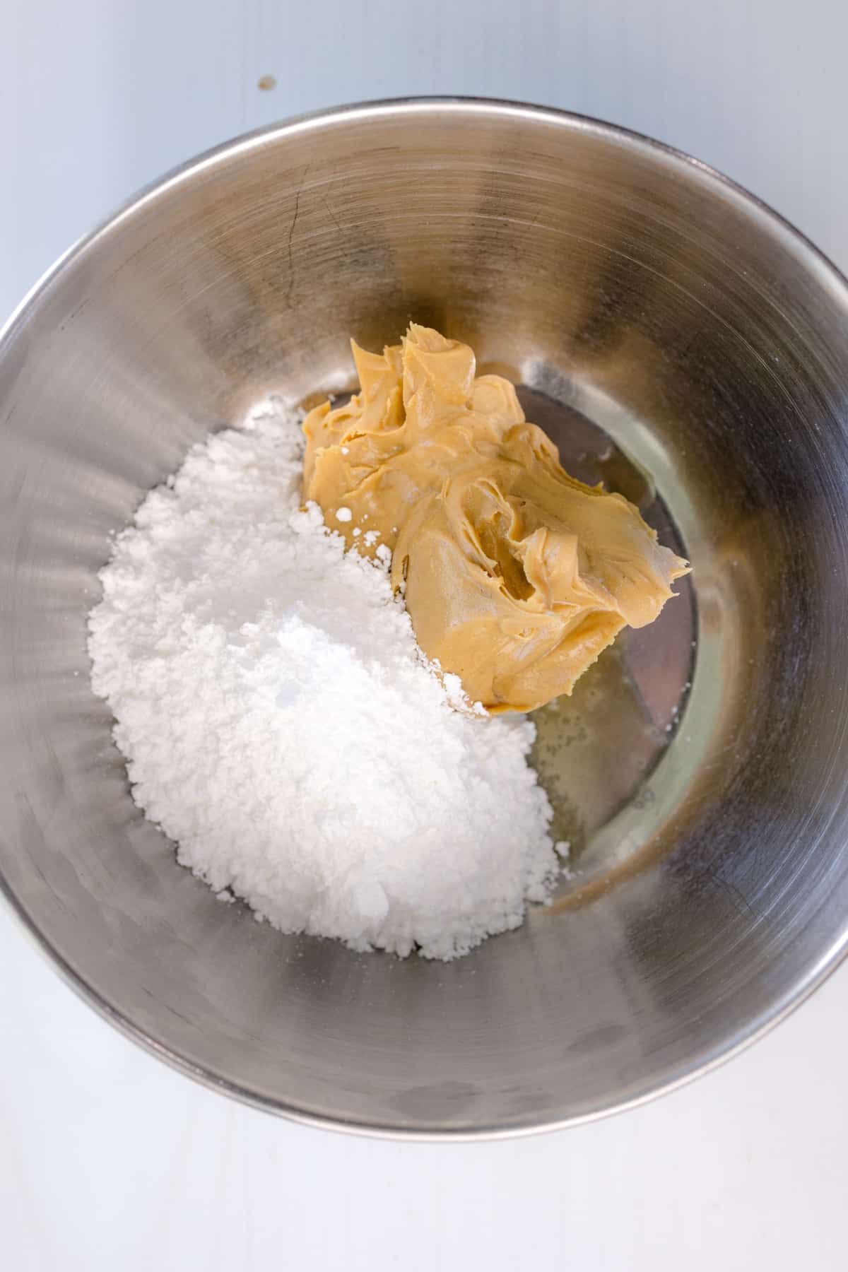 Close up shot of a mixing bowl with Peanut Butter, Powdered Sugar, and Vanilla Extract ready to be combined.