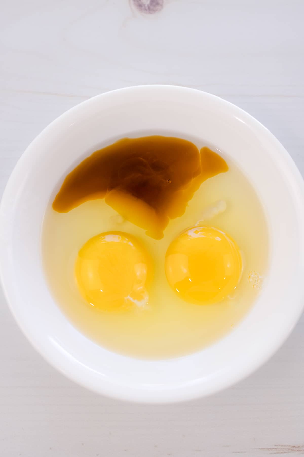 Overhead shot of eggs and vanilla extract in a small, white bowl.